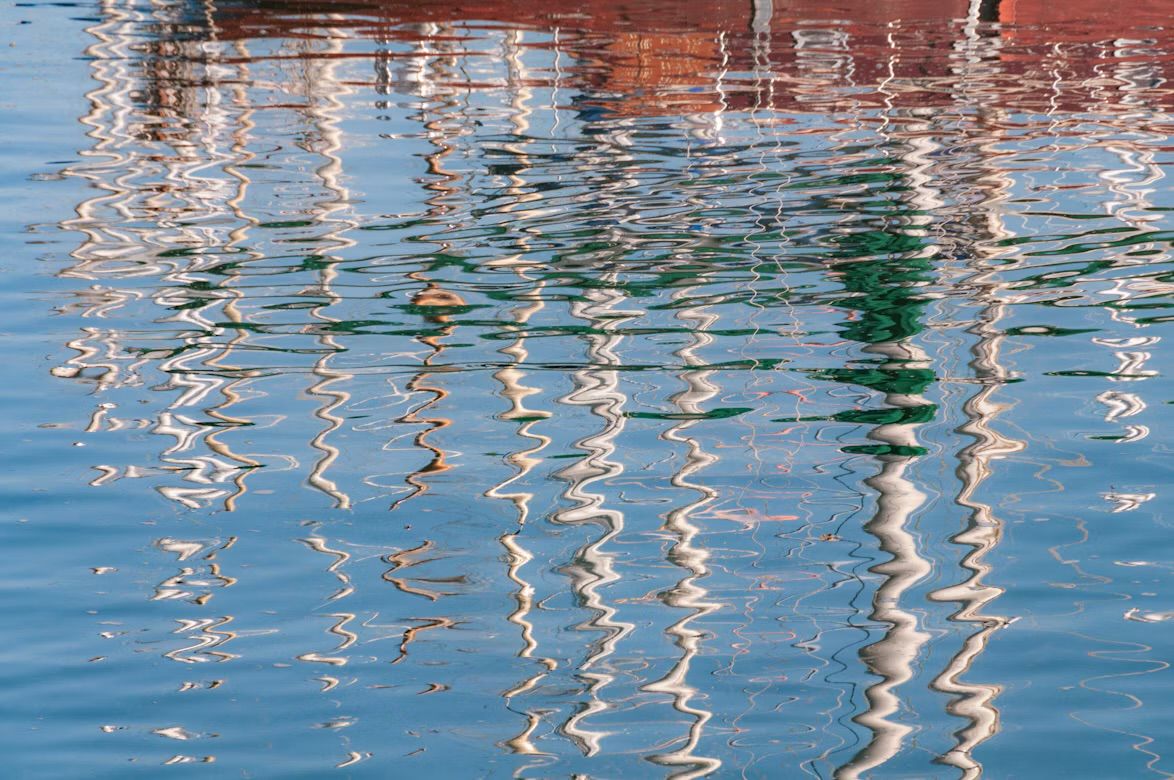 Reflections of boat masts rippling in the water of St Aubin's harbour, Jersey, Channel Islands.